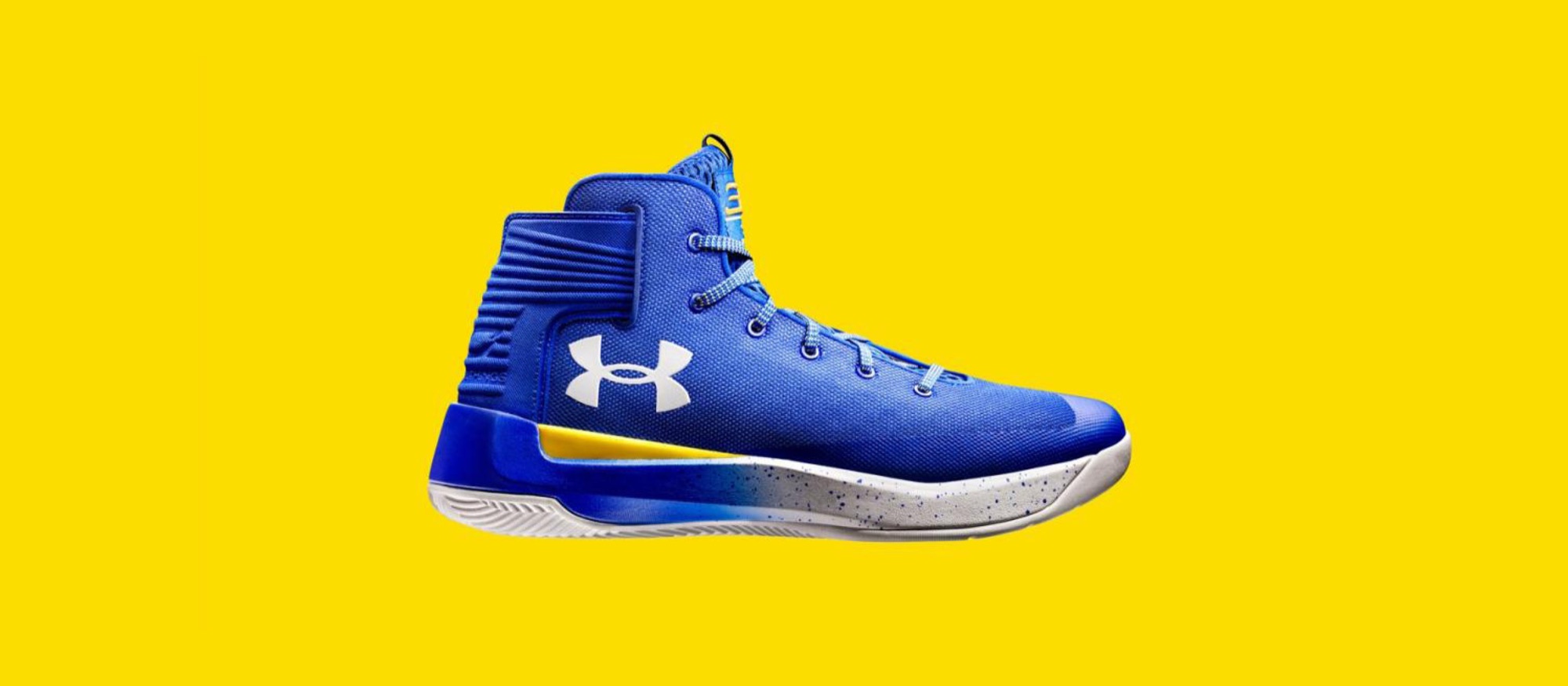 A royal blue Under Armour Curry basketball high-top on a yellow ground, the white logo on the side panel and a speckled white midsole