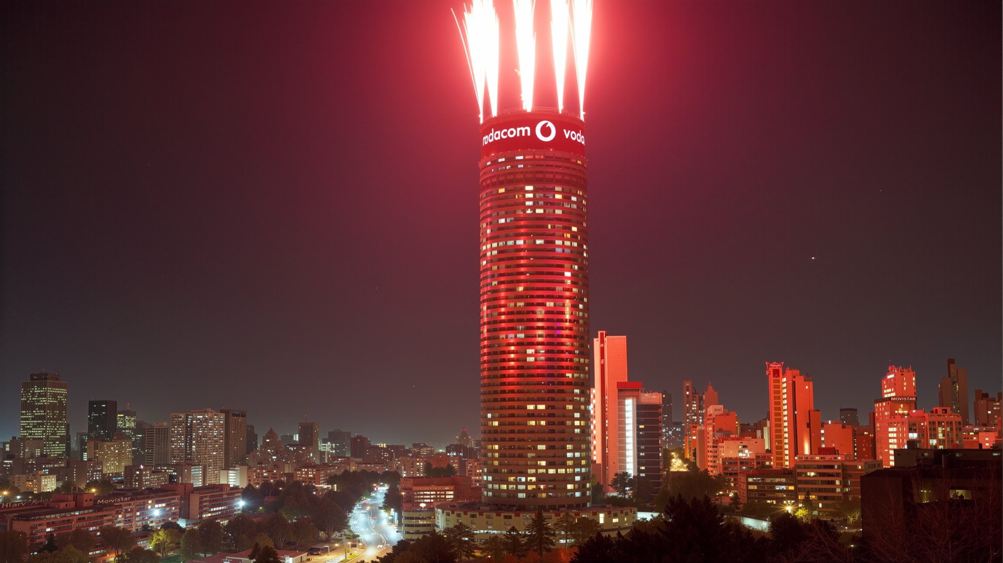 The Ponte tower in Johannesburg at night, its crown wrapped in a lit Vodacom sign with fireworks arcing from the roof above the city skyline